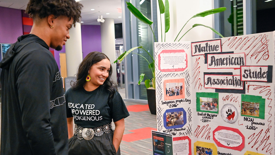 two students stand in front of a poster board for the Native American student association