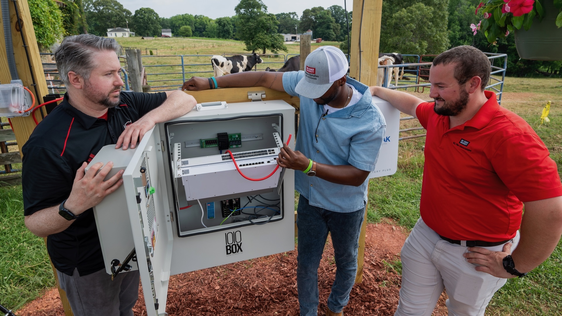 three men stand around internet equipment on a farm