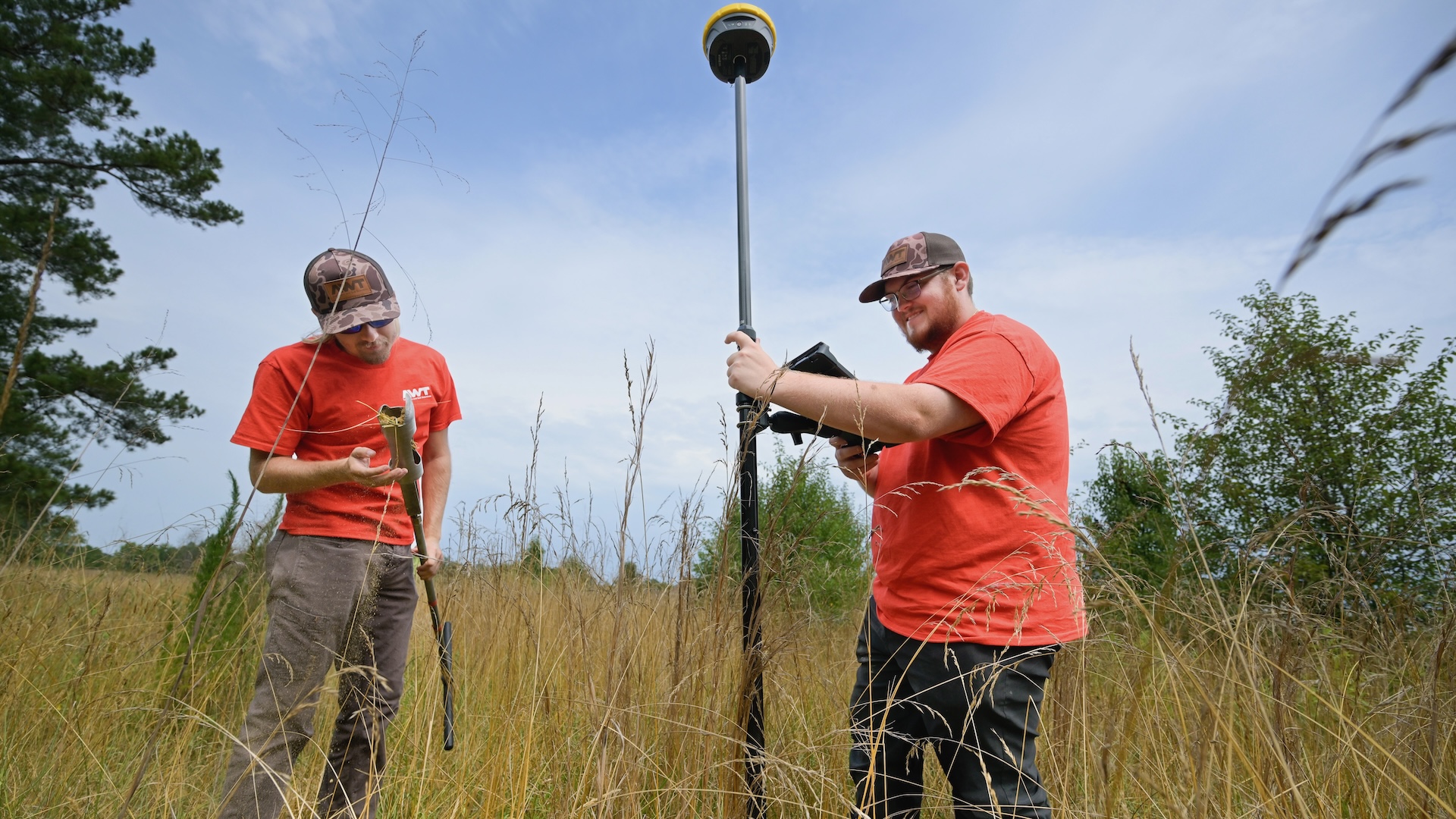 two men stand in a field with measuring equipment