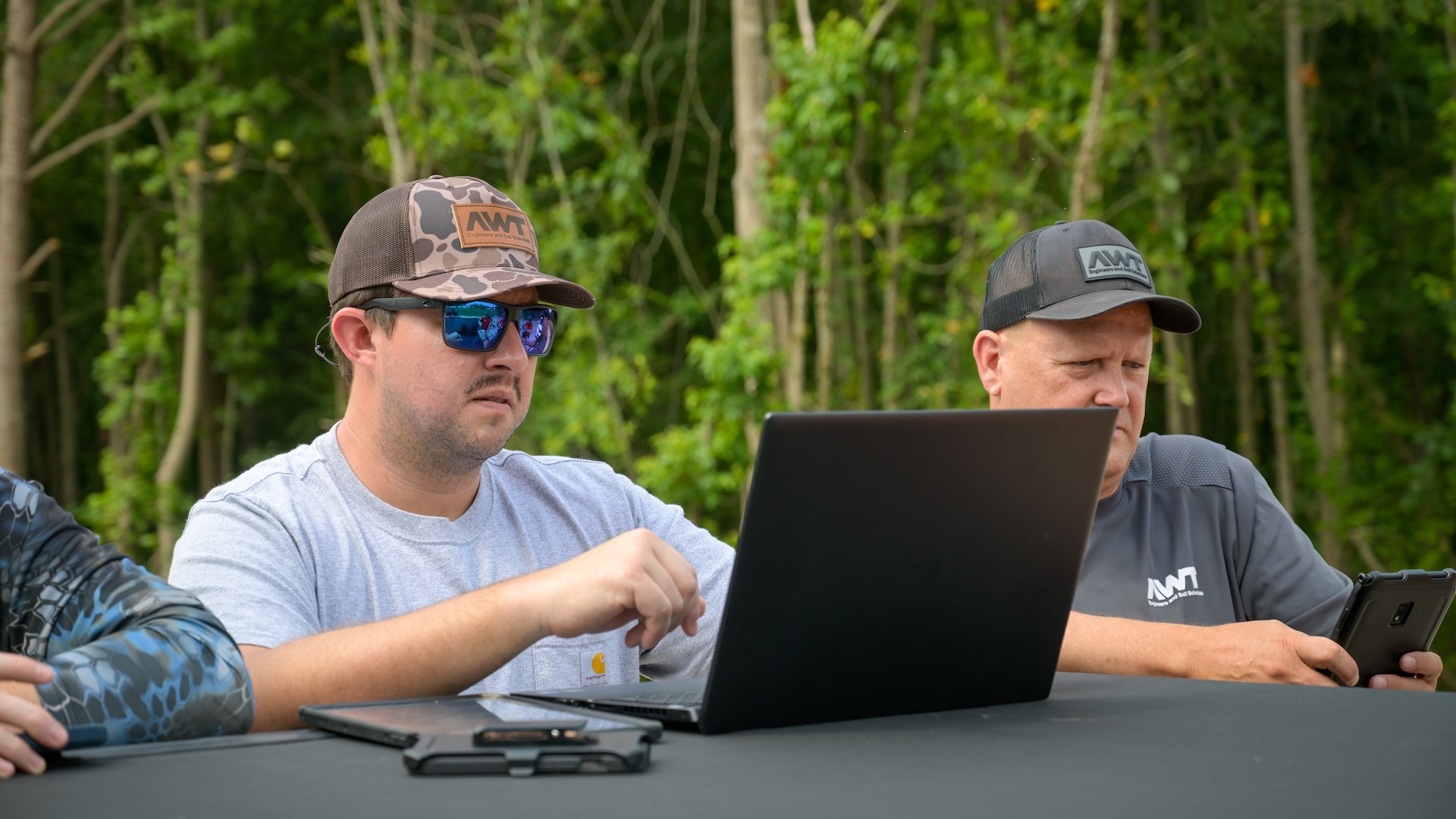 men look at laptops out in the field