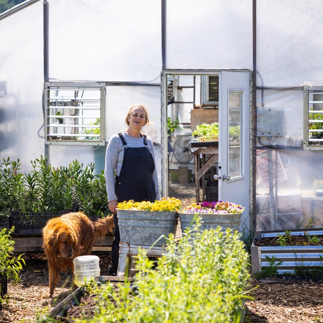 woman and dog standing outside a greenhouse
