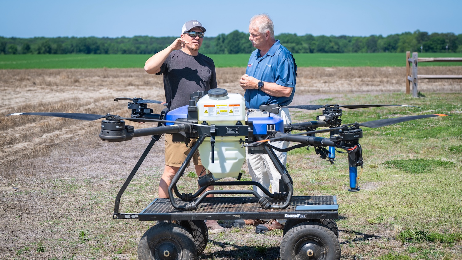a farmer and Extension agent stand in a farm field with a large drone