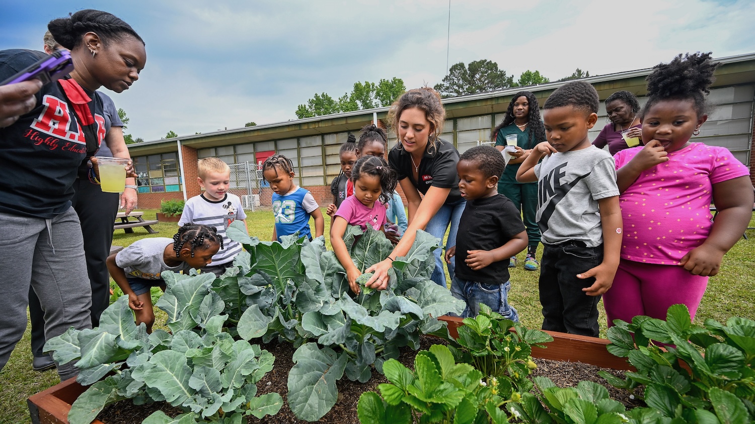 young kids and their teachers harvest produce from a community garden